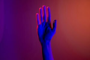 hand held up, lit by neon pink and purple light against a navy gradient backdrop.