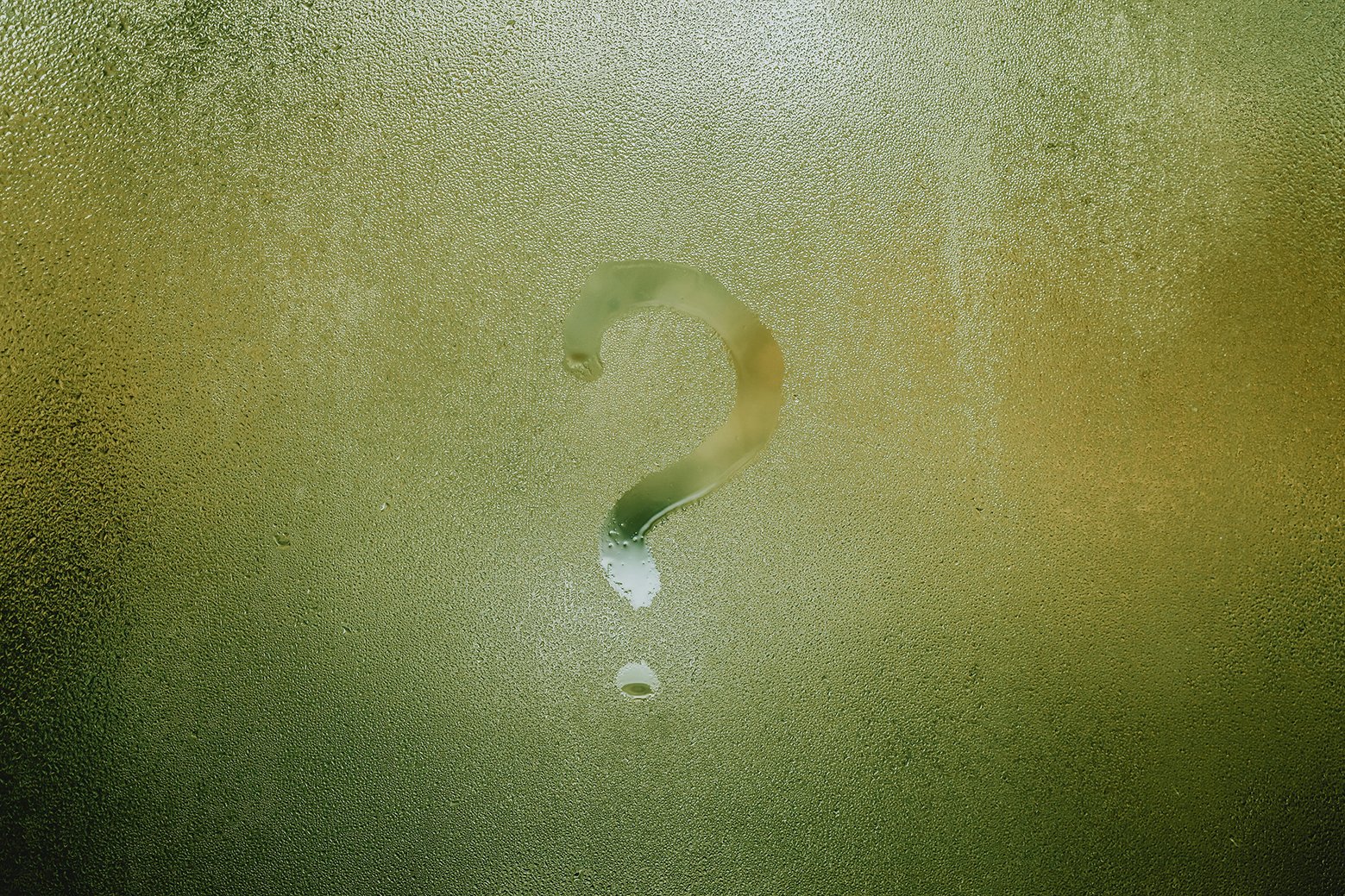 Question mark symbol drawn onto a foggy window with green poking through. Circular droplets of water are around the question mark.