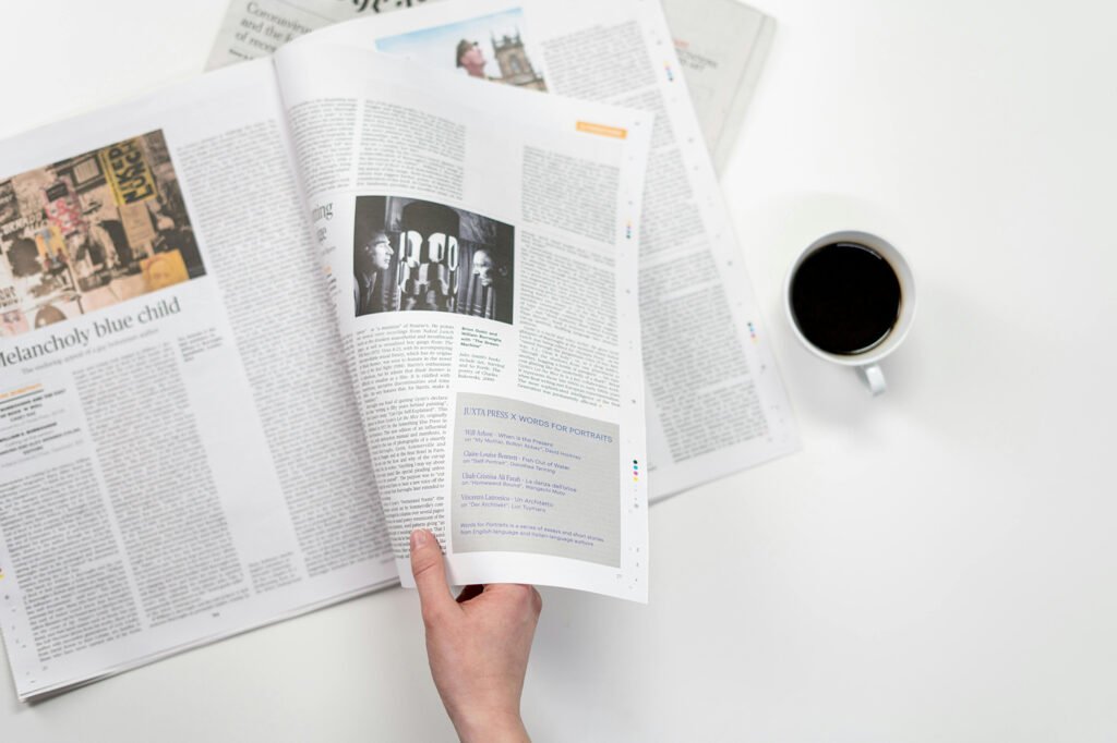 An open newspaper with a hand holding the right hand side and a cup of black coffee to the right of the image.