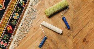 Two paint rollers on parquet flooring. One covered in green paint and one in cream.