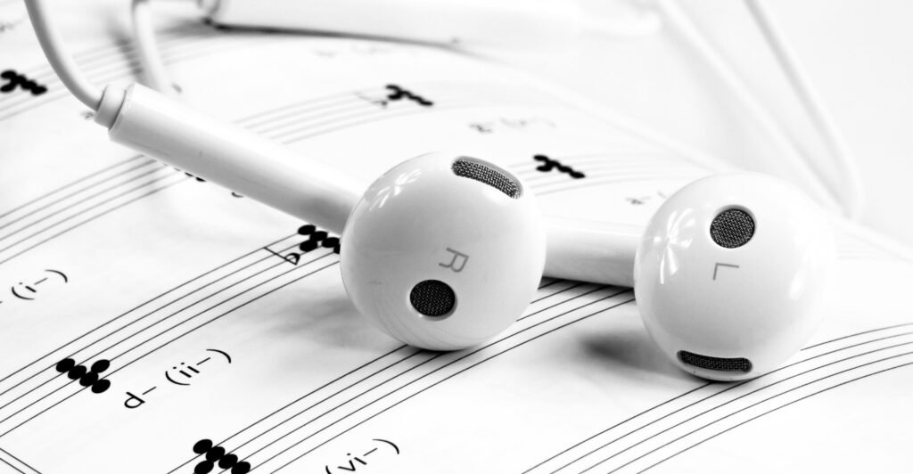 White wired apple earbuds laying on top of a sheet of music. You can see Left and Right marked on the side of the earbuds.