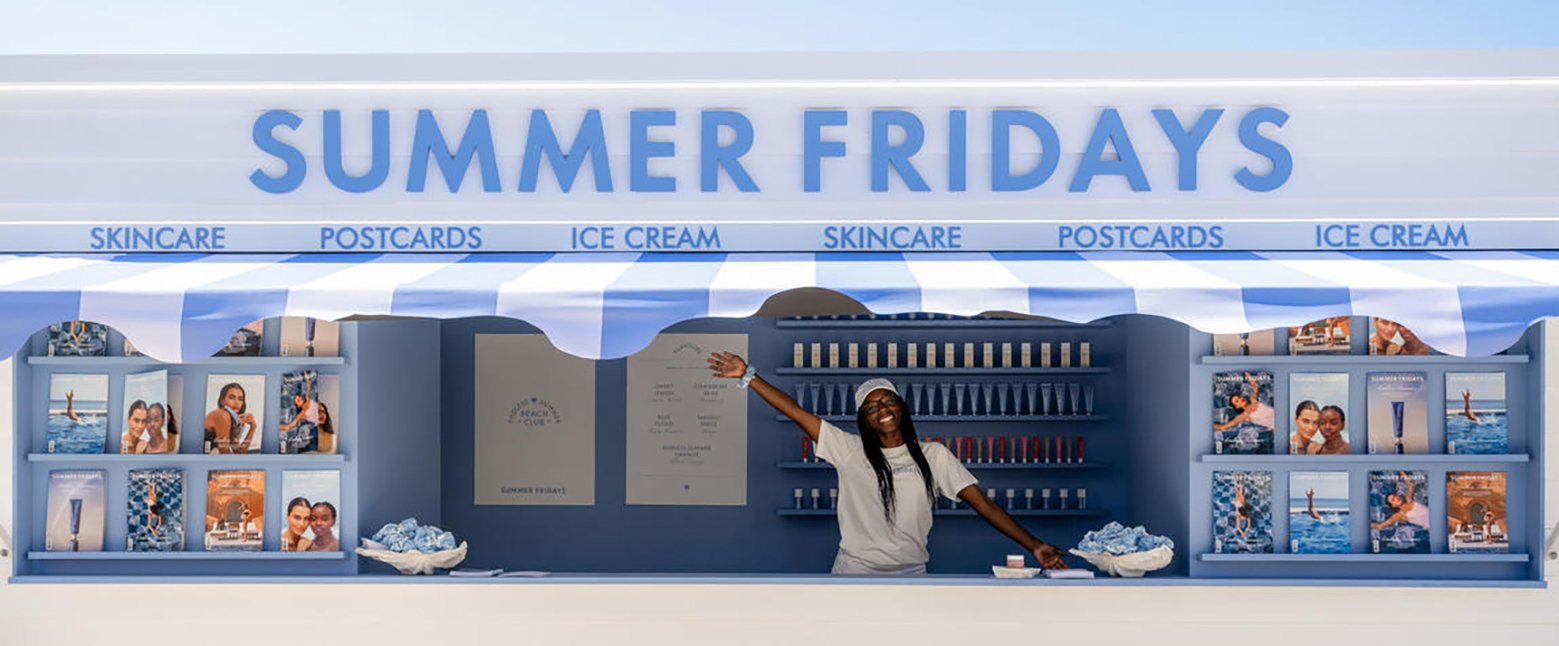 An ice cream pop-up set up by the beauty brand Summer Fridays in its pastel blue and white brand colours. A lady in a white t-shirt and hat has her arm stretched wide to welcome visitors.